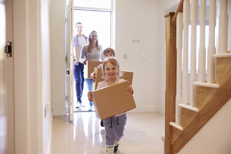 Familie mit Kindern trägt Umzugkisten durch die Tür. Umzug Haus Eigenheim shutterstock_451241899