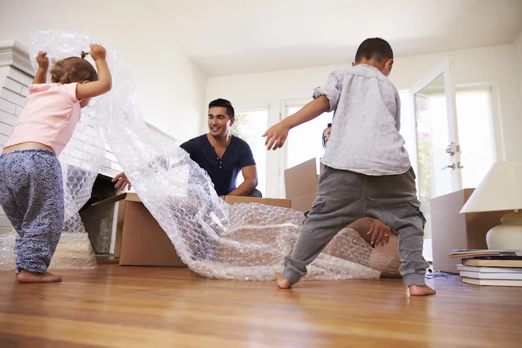 Familie mit zwei Kindern packt Kisten aus und spielt dabei mit Luftpolsterfolie.