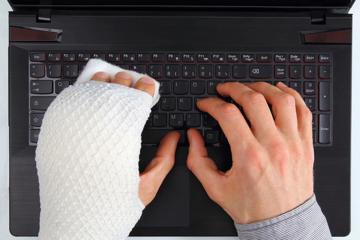 Zwei Hände auf Laptop-Tastatur, eine davon mit Gipsschiene