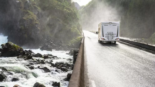 Ein Wohnmobil fährt auf einer straße neben einem Fluss oder Meer in einer Schlucht von grünen Bergen