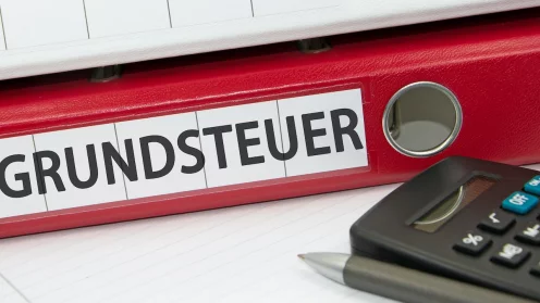 Ein roter Aktenordner auf dem Grundsteuer steht und ein Taschenrechner daneben