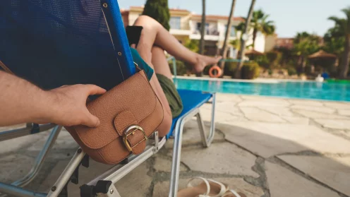 Eine Liege am Pool, an der eine Handtasche hängt. Eine Hand greift nach der Handtasche