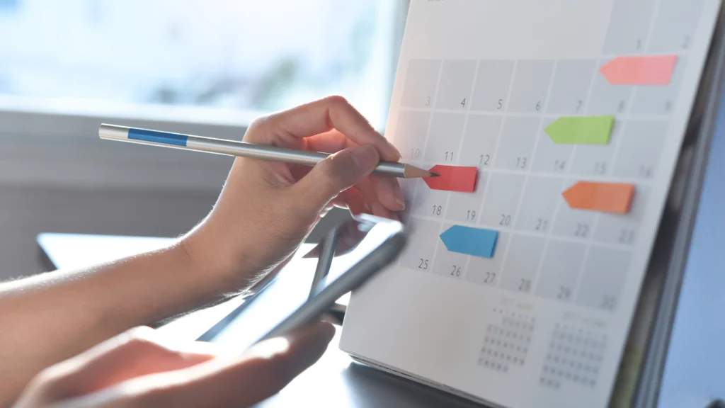 Hande, die mit einem Stift etwas in einen Kalender eintragen