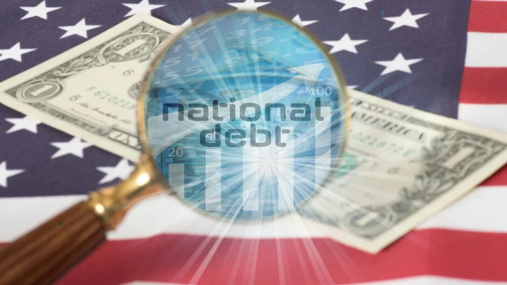 Lupe, durch der Schriftzug "Natonal Debt" platziert auf einer Dollarnote, die auf der US-Flagge liegt, zu sehen ist