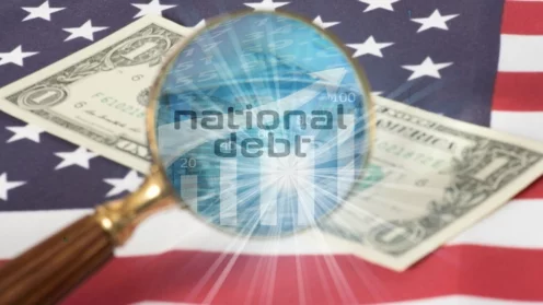 Lupe, durch der Schriftzug "Natonal Debt" platziert auf einer Dollarnote, die auf der US-Flagge liegt, zu sehen ist