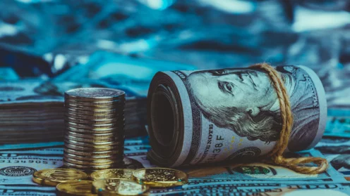 Eine Dollarrolle mit Münzen auf dem Hintergrund von verstreuten Hundert-Dollar-Scheinen in blauem Licht.
