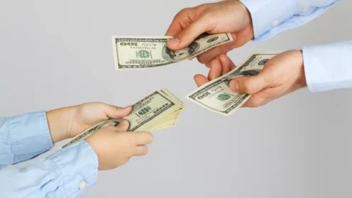 Männerhände geben den Jungenhänden Geld in Form von Hundert-Dollar-Scheinen. Geschäftsleute geben Geschäftsleuten Geld. Vater und Sohn.