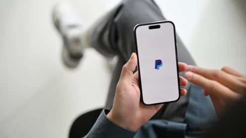 Nahaufnahme eines Mannes, der seine Rechnungen mit der mobilen PayPal-Anwendung bezahlt. iPhone mit PayPal Logo auf dem Bildschirm.