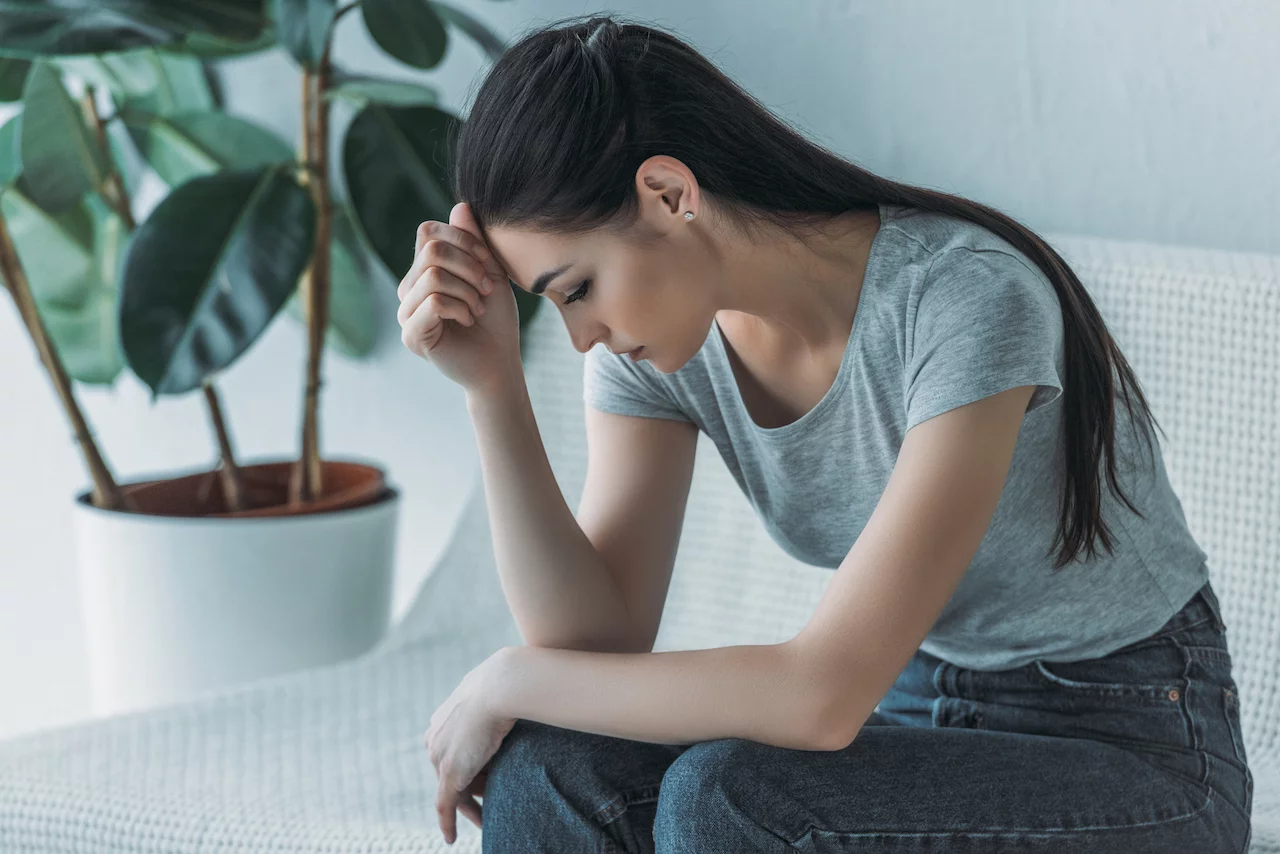 Frustrierte junge Frau in Depressionen sitzt auf Couch und schaut nach unten