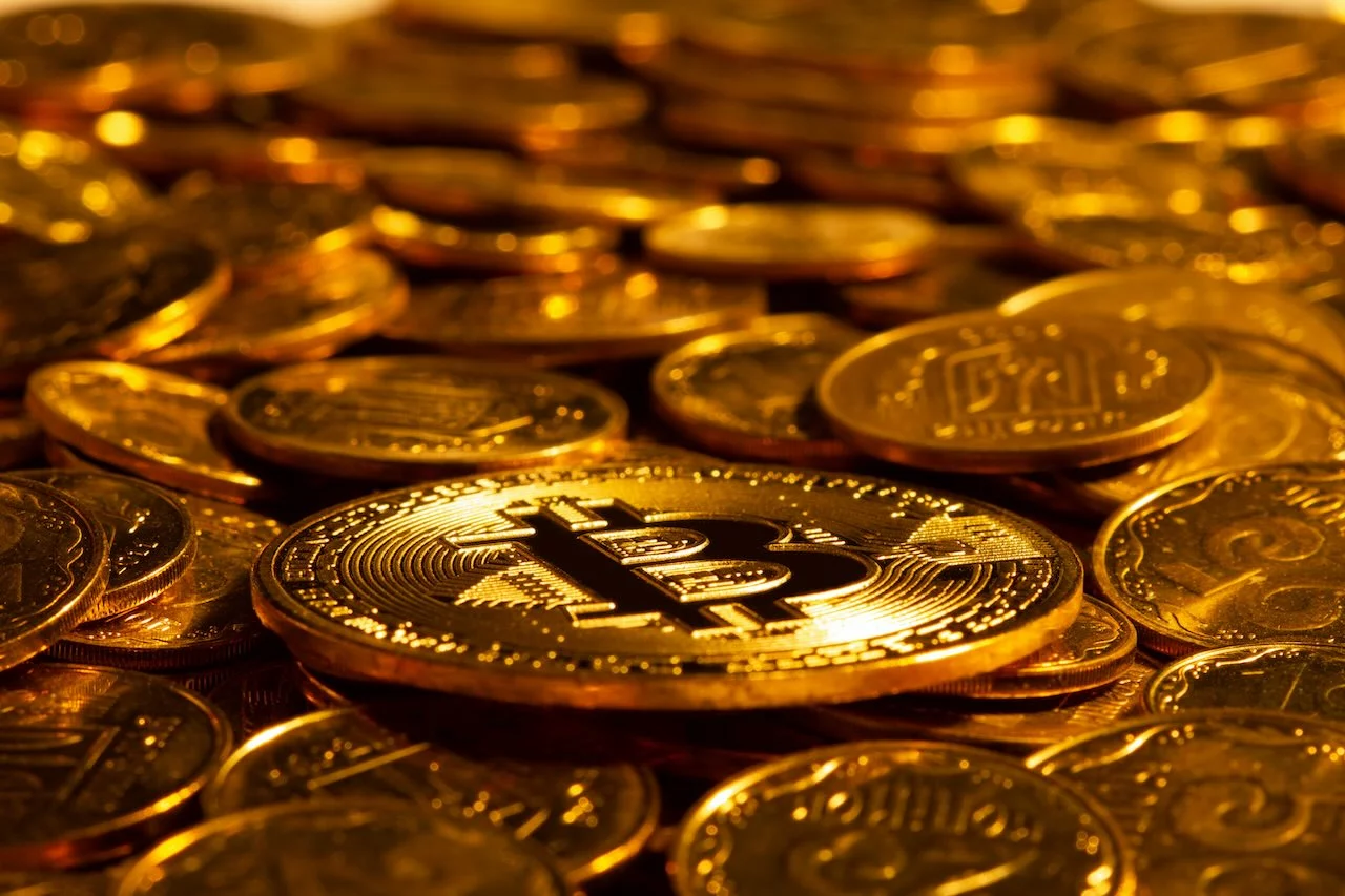Gold Kryptowährung Bitcoin vor dem Hintergrund vieler anderer Goldmünzen in hartem Licht. Neues Konzept des steigenden Wertes der digitalen Kryptowährungen der Blockchain-Branche. Nahaufnahme.