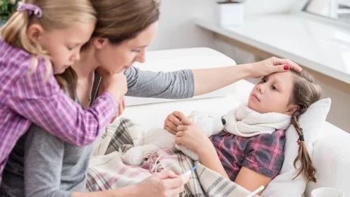 Mutter sitzt am Krankenbett der kranken Tochter und misst die Temperatur