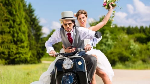 Hochzeitspaar fährt Motorroller in Hochzeitskleid und Anzug