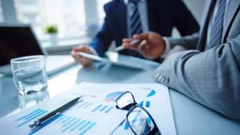 Image of eyeglasses and financial documents at workplace with businessmen discussing ideas near by