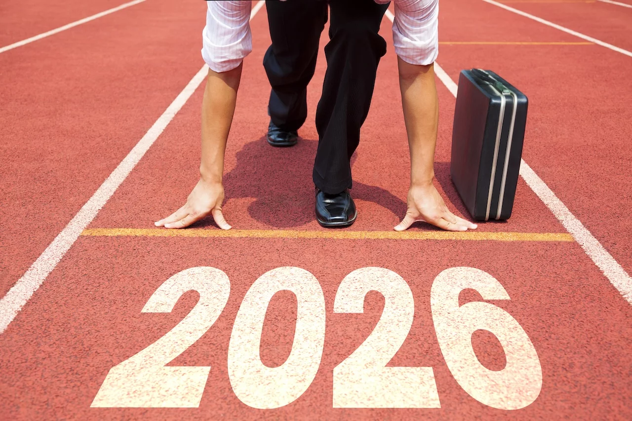 Konzept „Frohes neues Jahr 2026“. Geschäftsmann, der sich auf einer Leichtathletikbahn mit der Jahreszahl 2026 darauf vorbereitet, loszulaufen.
