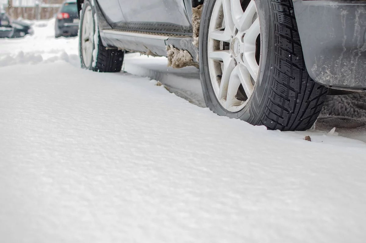 Nahaufnahme eines Autoreifens auf einer schneebedeckten Winterstraße. Auf dem Gummirad liegen Schneeflocken; Kfz; Kfz-Versicherung, Winter