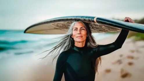 Senior-Suferin schultert ihr Surfbrett