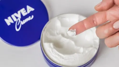 Geöffnete Dose Nivea Creme mit entnommener Hautcreme auf einer Fingerspitze.