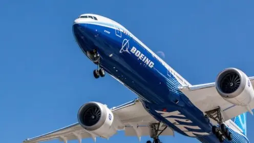 Eine Boeing-Passagiermaschine mit Boeing-Schriftzug ist von schräg unten vor tiefblauem Himmel im Gegenlicht zu sehen.