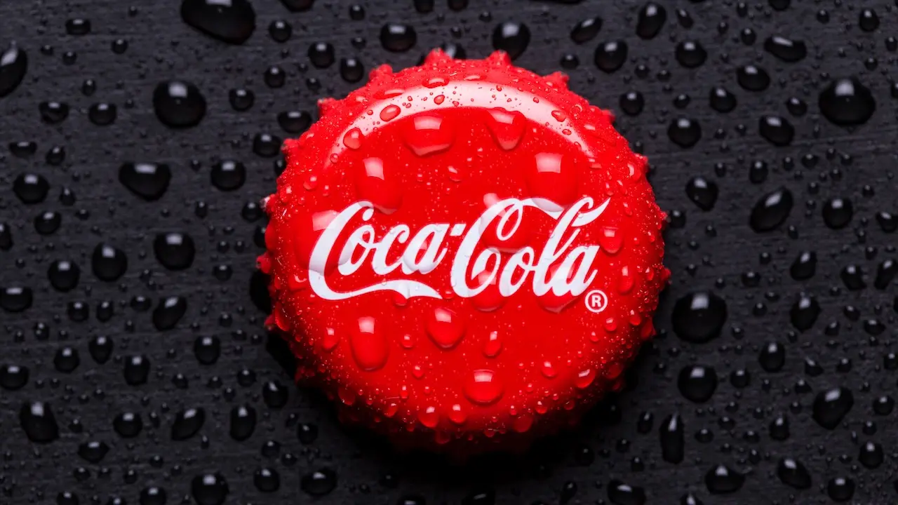 Ein roter Coca-Cola-Kronkorken mit weißen Logo und Wassertropfen.
