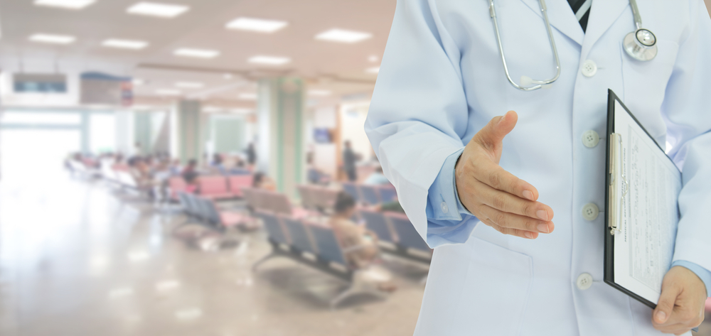 Mann im Arztkittel reicht die Hand im Warteraum eines Krankenhauses