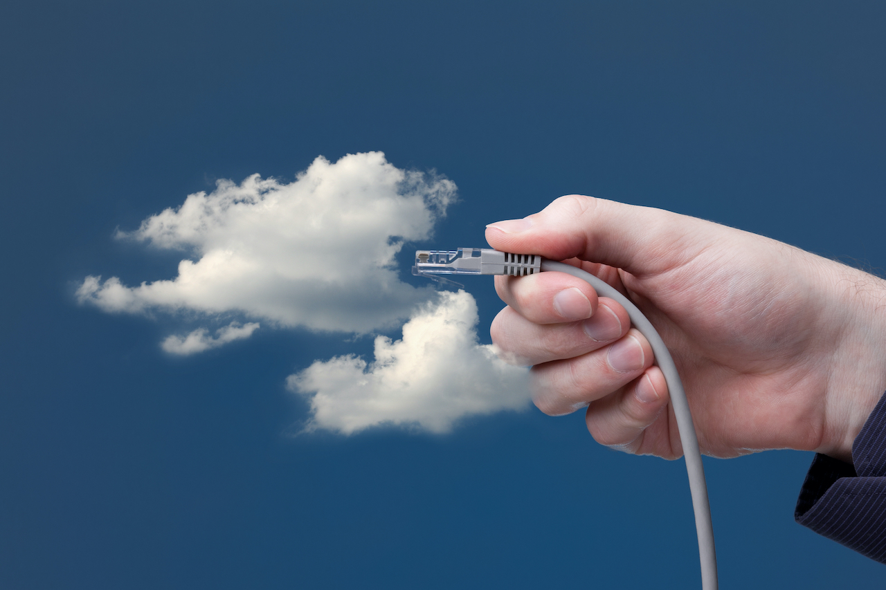 Eine weiße Wolke auf blauem Hintergrund und davor hält eine Hand einen Stecker