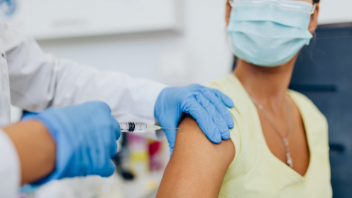 Zwei Hände in blauen Handschuhen verabreichen eine Impfung in einen Oberarm.