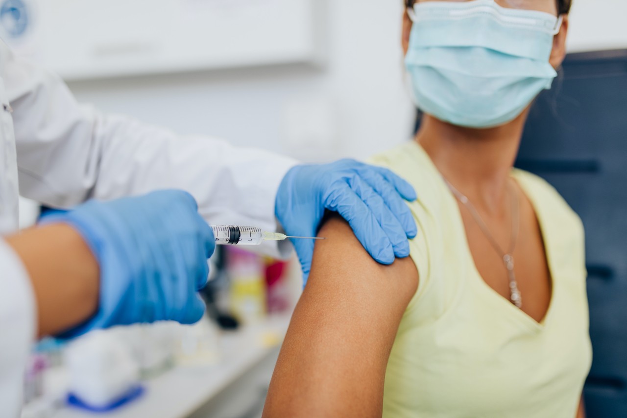 Zwei Hände in blauen Handschuhen verabreichen eine Impfung in einen Oberarm.