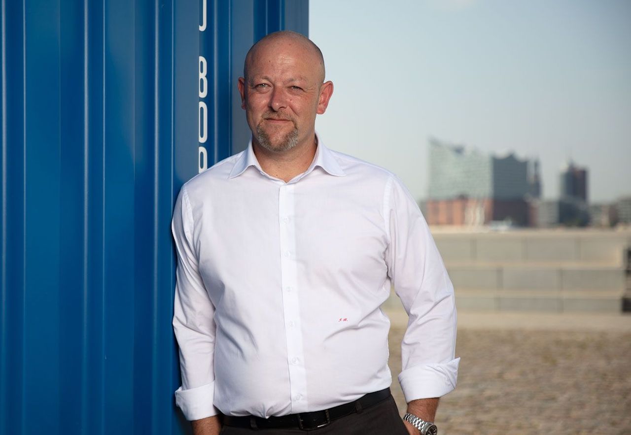 Solvium Geschäftsführer Jürgen Kestler lehnt an einem Container, im Hintergrund die Hamburger Elbphilharmonie