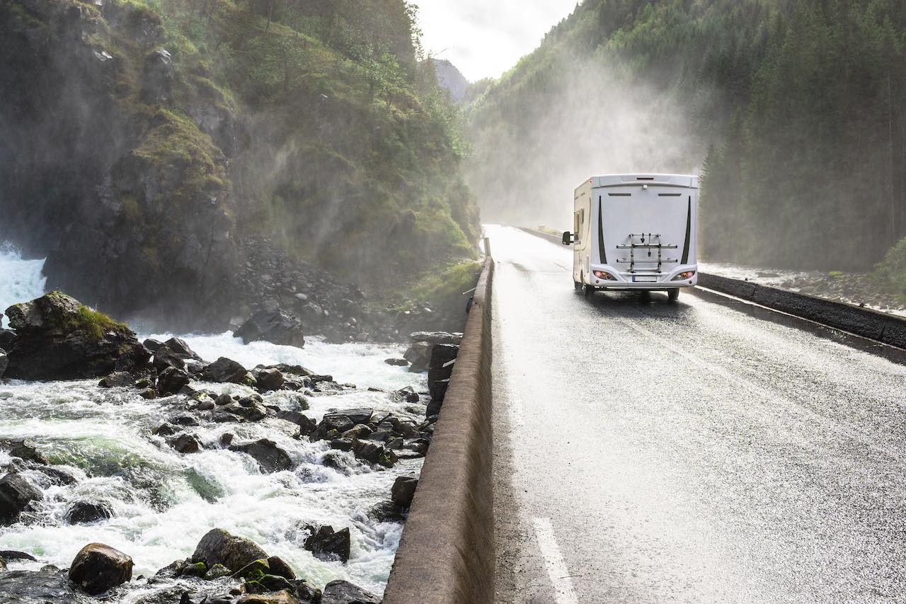 Ein Wohnmobil fährt auf einer straße neben einem Fluss oder Meer in einer Schlucht von grünen Bergen