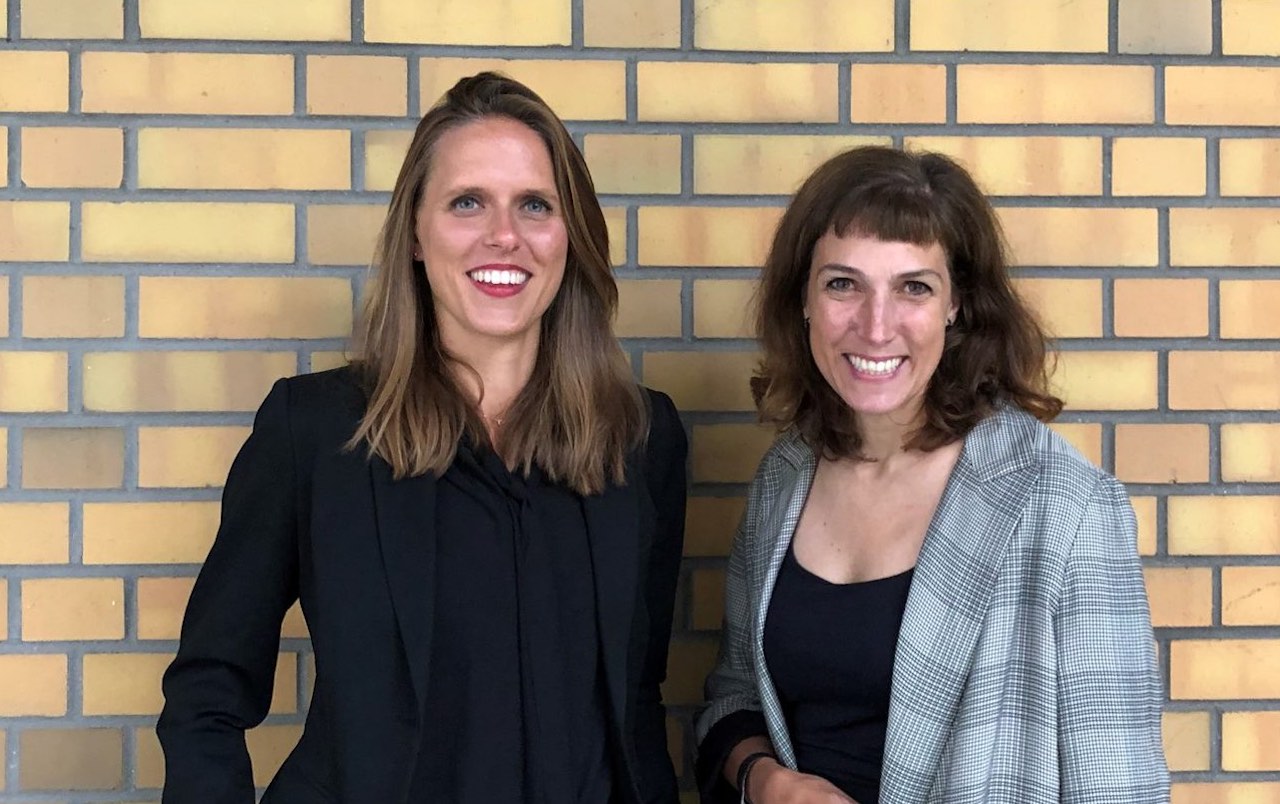 Sophie Kazmierczak und Tanja Volksheimer von der Bundesinitiative Impact Investing vor einer gelben Backstein-Wand..