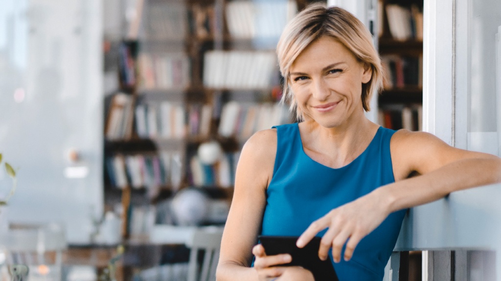 Bild einer lächelnden Frau mit Smartphone vor Bücherwand