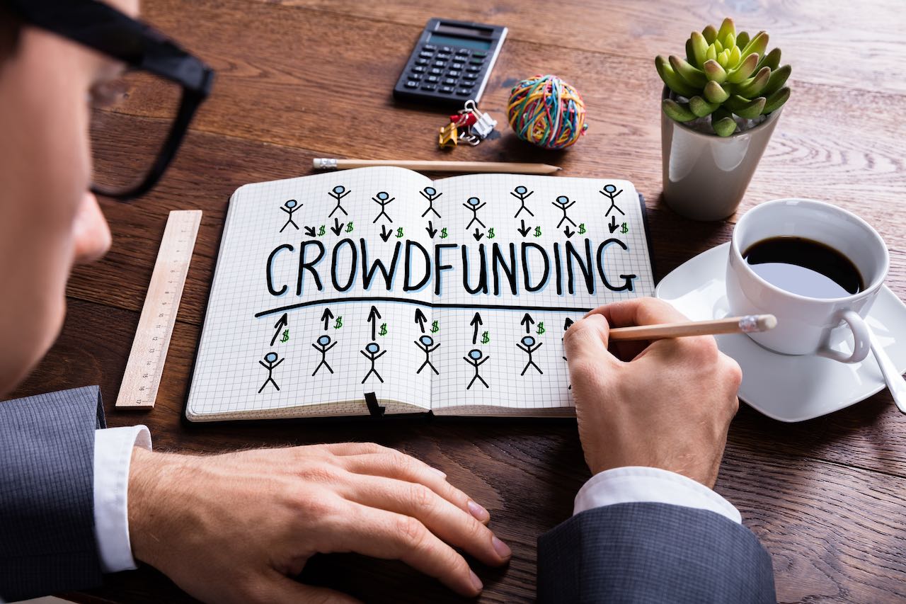 Ein Mann zeichnet in einem Heft mit dem Wort Crowdfunding.