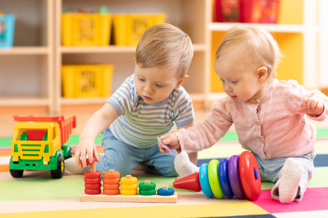 Zwei Babys sitzen vor buntem Holzspielzeug