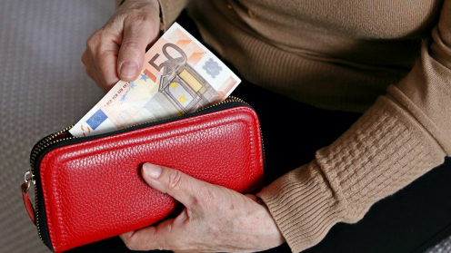 Ältere Hände die ein rotes Portemonnaie halten, aus dem Geldscheine genommen werden
