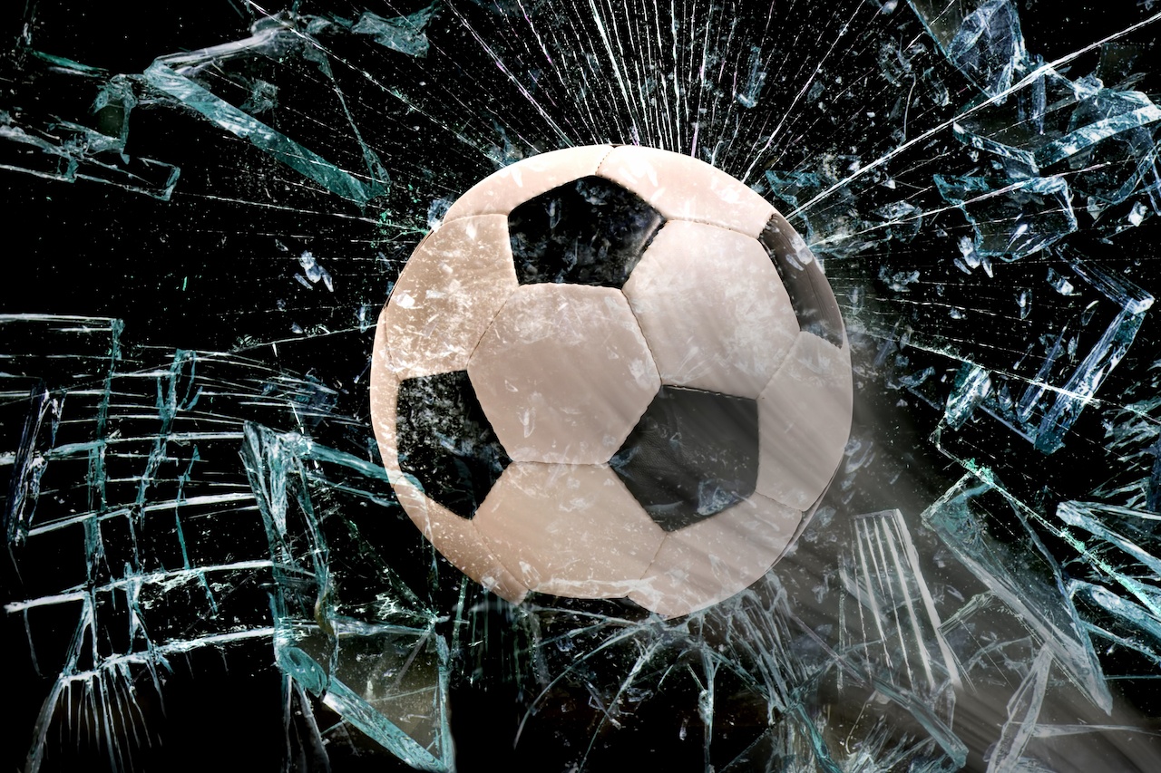 Ein Fußball fliegt in eine Scheibe, die zerbricht