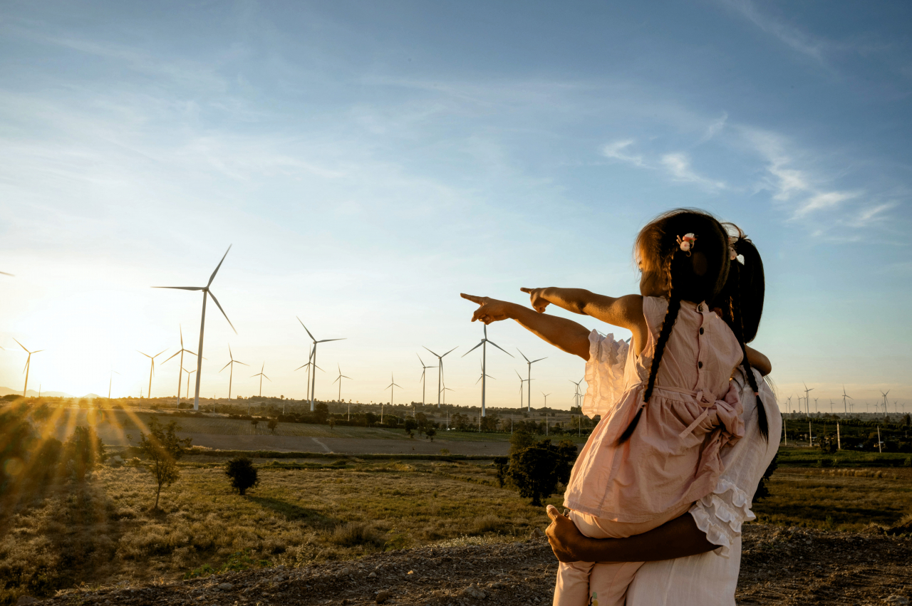 Mutter mit Kind auf dem Arm beide stehen draußen und zeigen auf Windräder