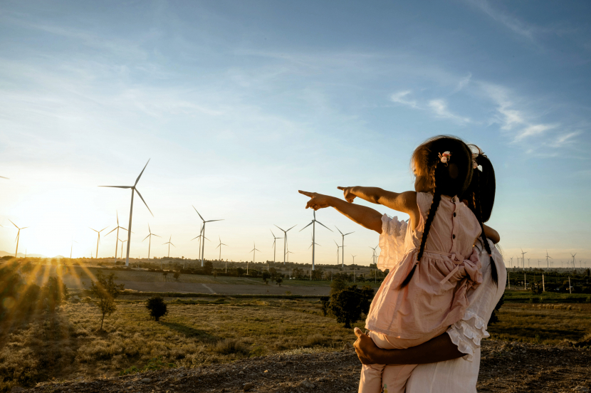 Mutter mit Kind auf dem Arm beide stehen draußen und zeigen auf Windräder