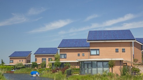 Häuser an einem Wasserlauf, deren Dächer Solarplatten tragen