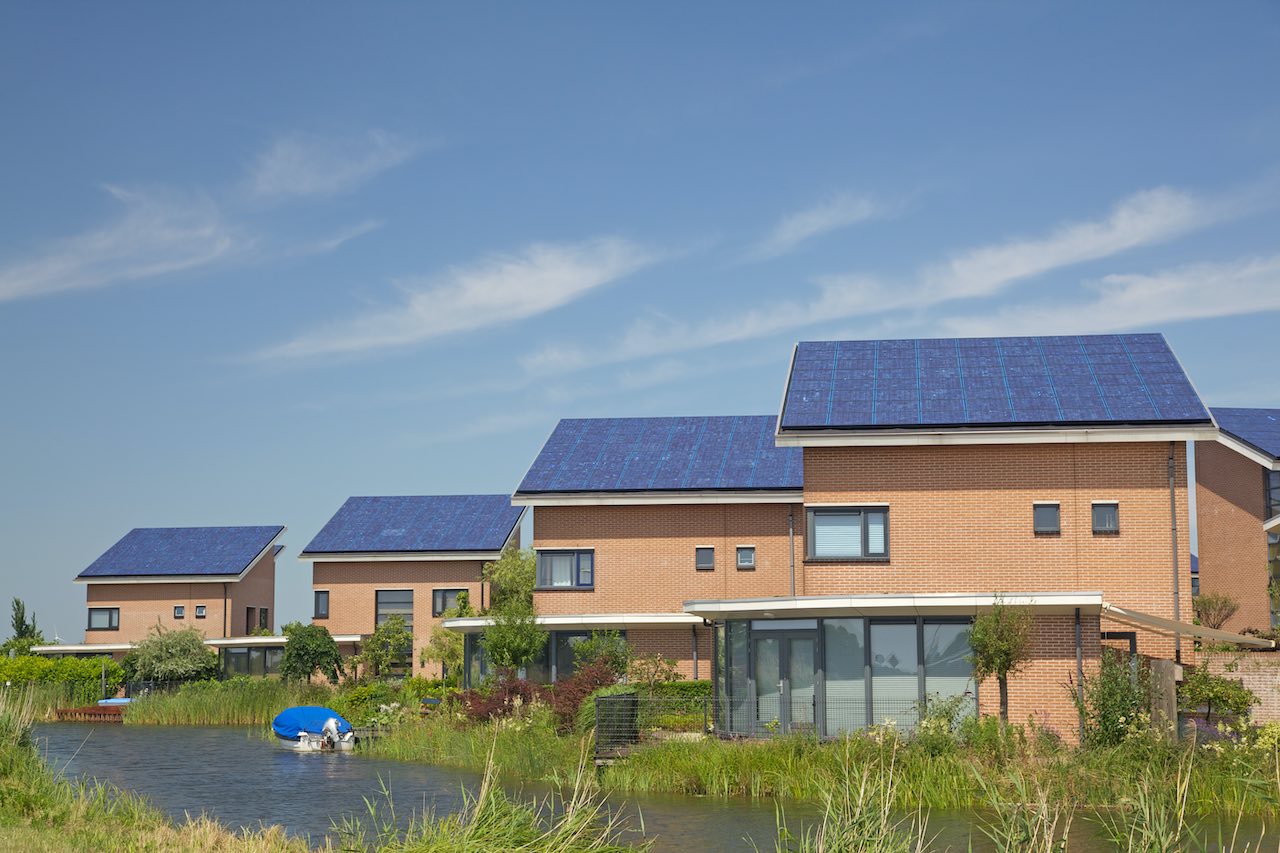 Häuser an einem Wasserlauf, deren Dächer Solarplatten tragen