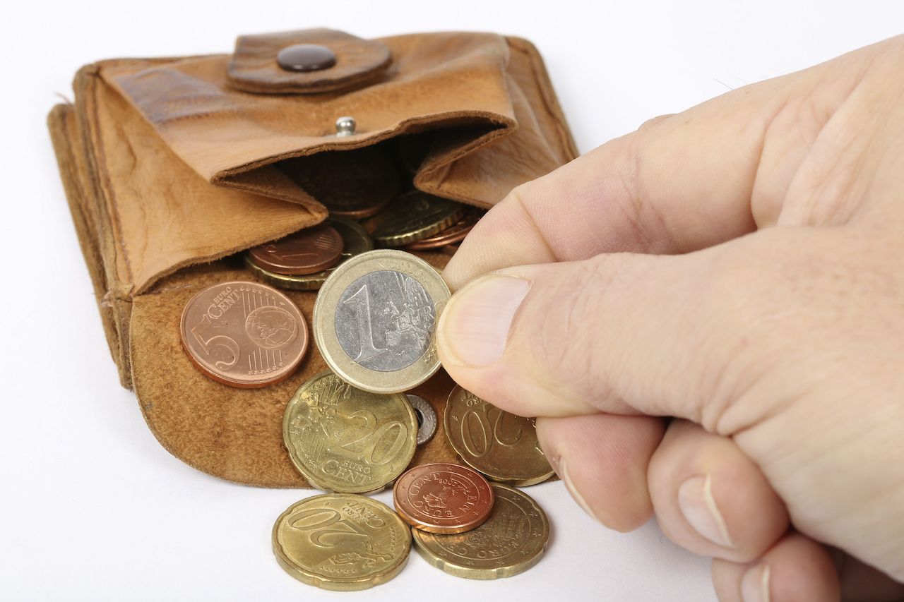 Eine ausgekippte Geldbörse aus der Münzen fallen und eine Hand nimmt einen Euro