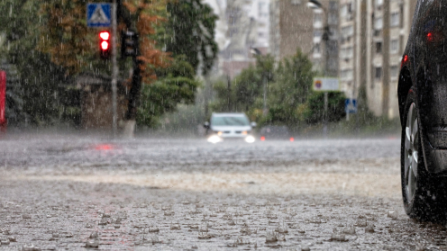 Starregen prasselt auf eine überflutete Straßen. In großer Entfernung sieht man ein Auto im Wasser entgegenkommen