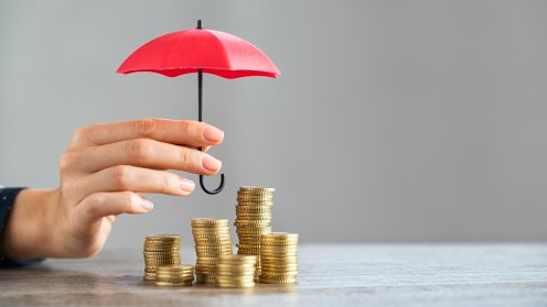 Ein kleiner roter Regenschirm wird über Geldhäufchen gehalten