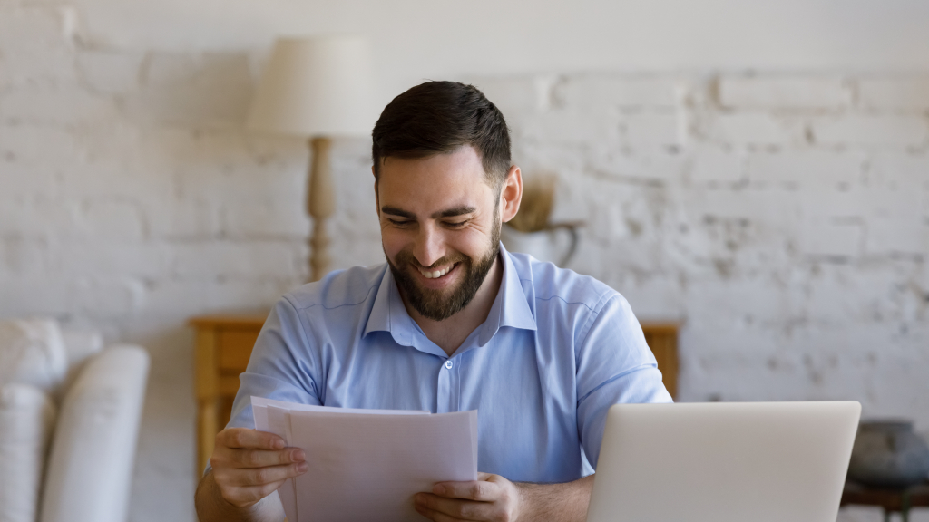 Mann sitzt am Tisch und lächelt über einen Brief, den er in der Hand hält
