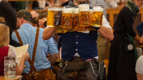 Ein Kellner in Traditionskleidung trägt viele Maß Bier auf dem Oktoberfest