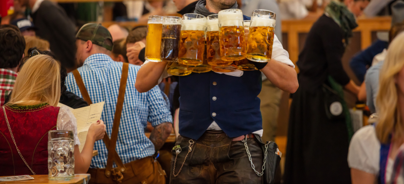 Ein Kellner in Traditionskleidung trägt viele Maß Bier auf dem Oktoberfest