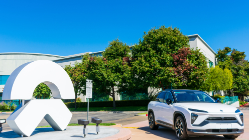 Ein weißer SUV der Marke NIO neben dem Firmenlogo von NIO