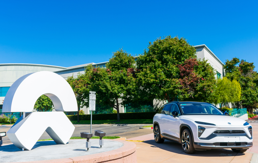 Ein weißer SUV der Marke NIO neben dem Firmenlogo von NIO