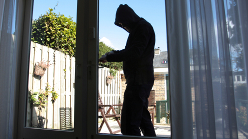 Ein Mann mit dunklem Kapuzenpulli bricht in eine Terrassentür ein
