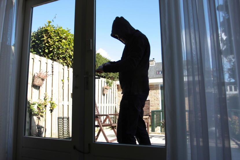 Ein Mann mit dunklem Kapuzenpulli bricht in eine Terrassentür ein
