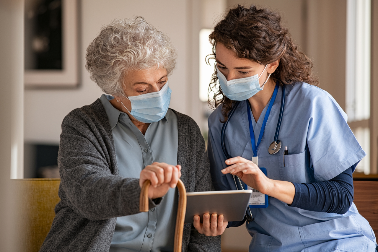 Alte Frau steht neben einer Krankenschwester und beide schauen auf ein Tablet